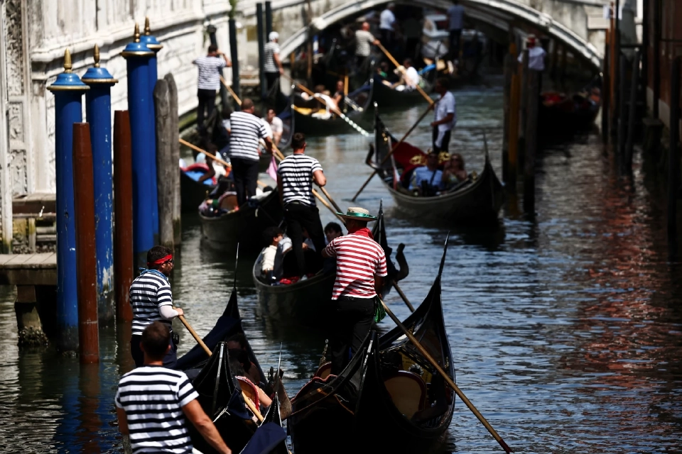 คนพายเรือกอนโดลาล่องไปตามคลองเวนิสเพื่อเตรียมเข้าพิธีวิวาห์ระหว่างผู้ก่อตั้ง Amazon เจฟฟ์เบโซสและลอเรน ซานเชซ ในเมืองเวนิส ประเทศอิตาลี เมื่อวันที่ 22 มิถุนายน 2025 REUTERS