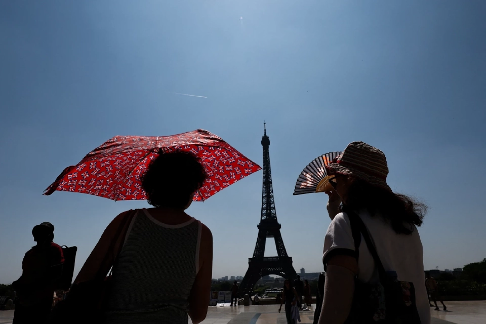 นักท่องเที่ยวปกป้องตัวเองจากแสงแดดใกล้หอไอเฟลในวันที่อากาศอบอุ่นและมีแดดในฤดูใบไม้ผลิที่กรุงปารีส ประเทศฝรั่งเศส 